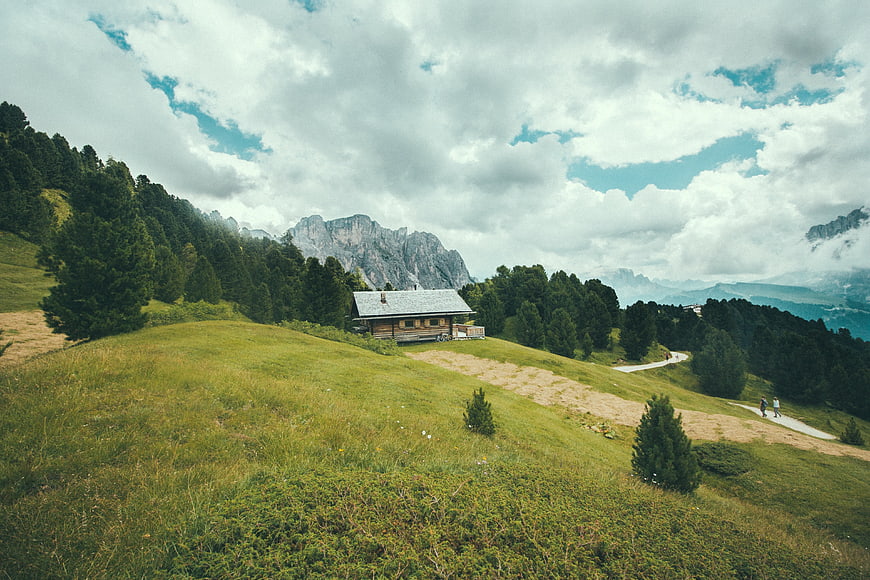 Alpine wooden cabin on grassy hill with mountains