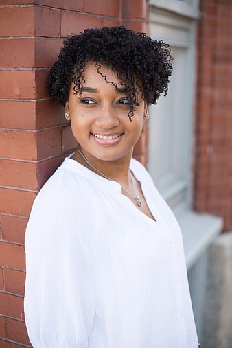 Smiling young woman with curly hair leaning against brick wall