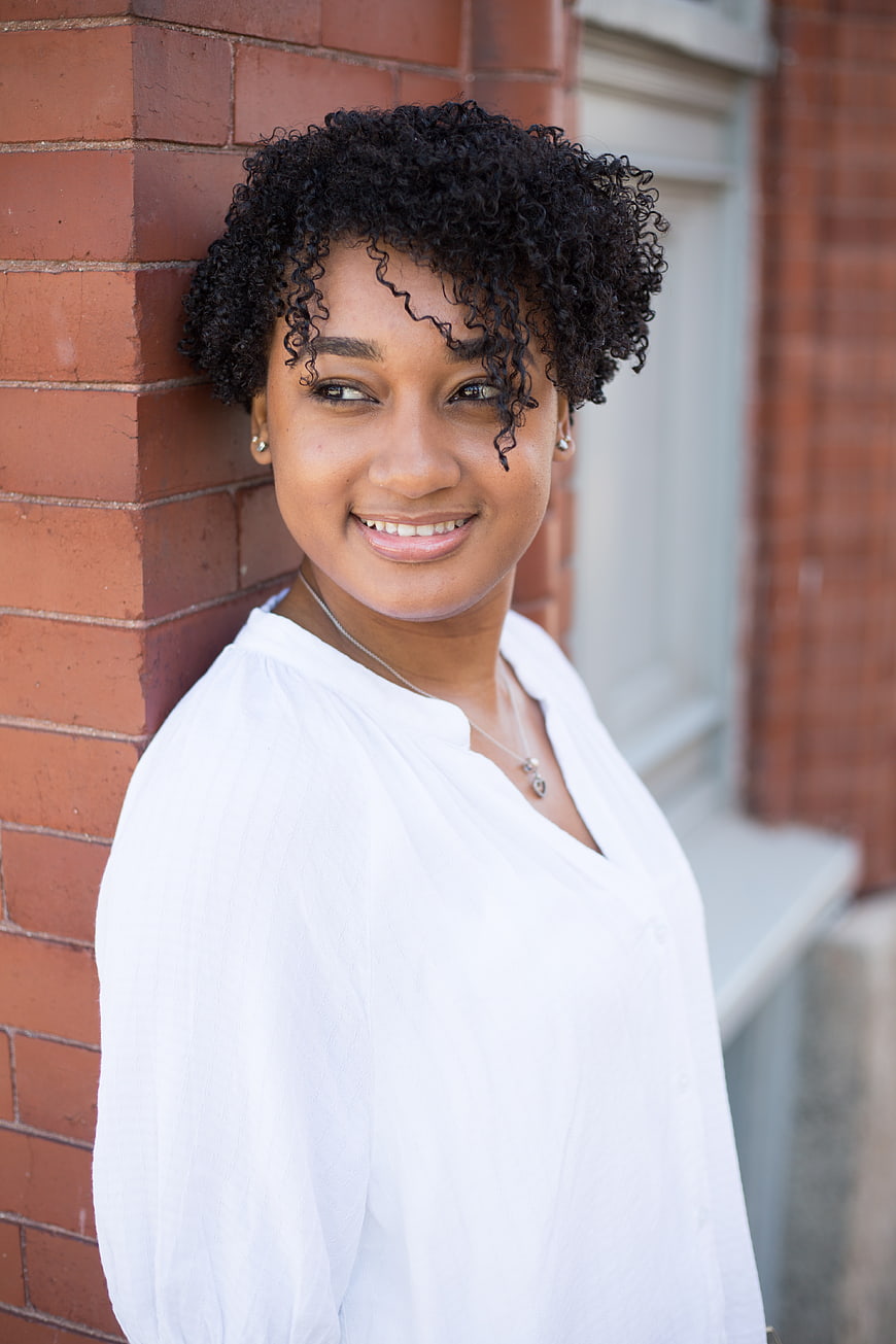 Smiling young woman with curly hair leaning against brick wall