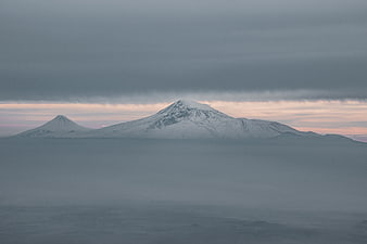 Snowy mountain peaks rising above a sea of clouds at dusk