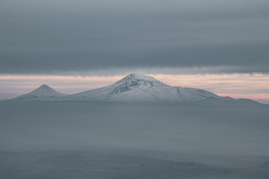 Snowy mountain peaks rising above a sea of clouds at dusk