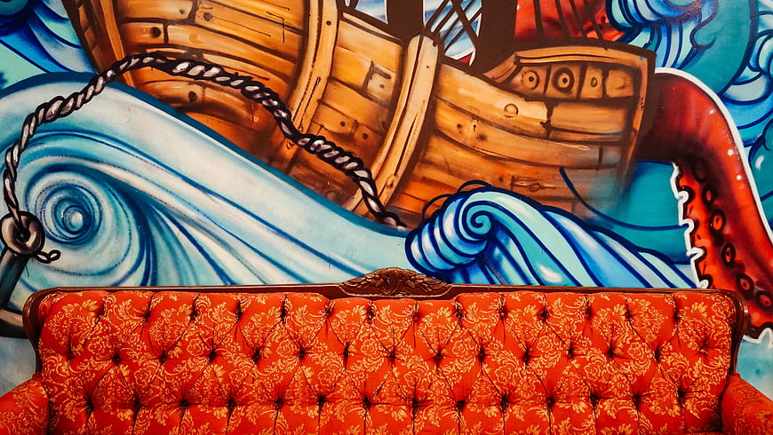 Orange tufted sofa against vibrant pirate ship mural