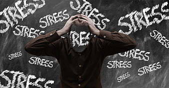 Stressed man holding head in front of blackboard with stress words