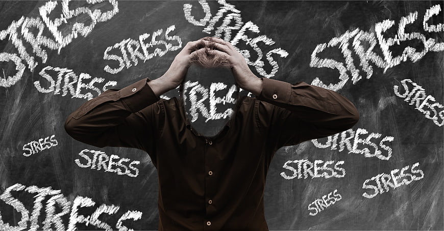Stressed man holding head in front of blackboard with stress words
