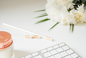 Minimalist white desk with keyboard, flowers, and beauty products
