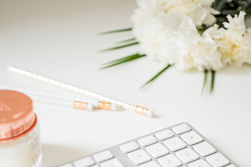 Minimalist white desk with keyboard, flowers, and beauty products