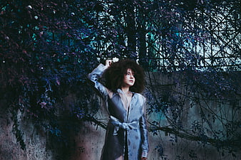 Woman with curly hair in blue robe against ivy wall