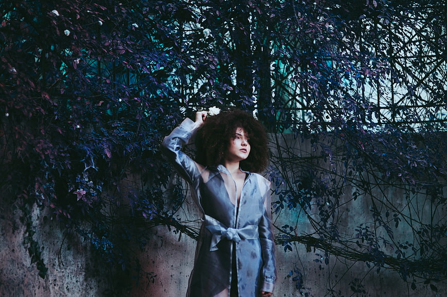 Woman with curly hair in blue robe against ivy wall