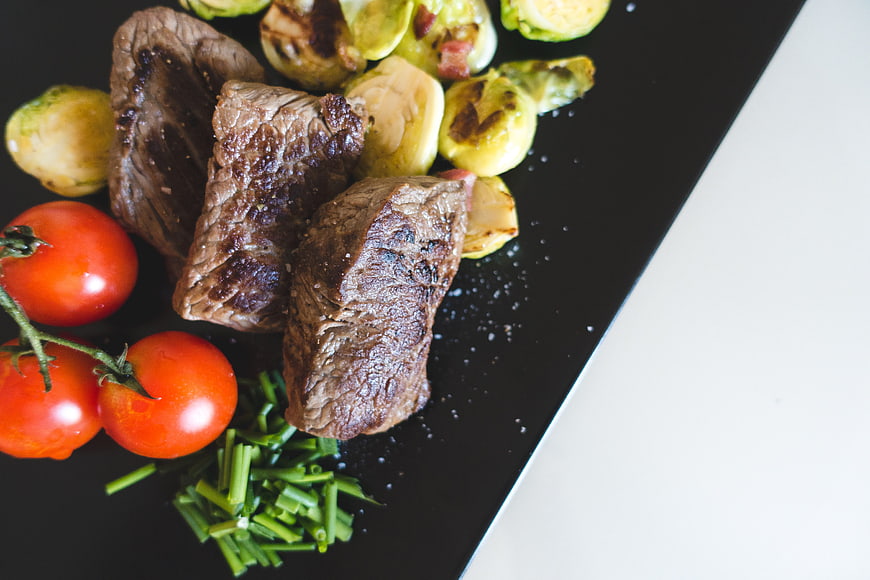 Grilled Beef Steak with Brussels Sprouts and Tomatoes on Black Plate