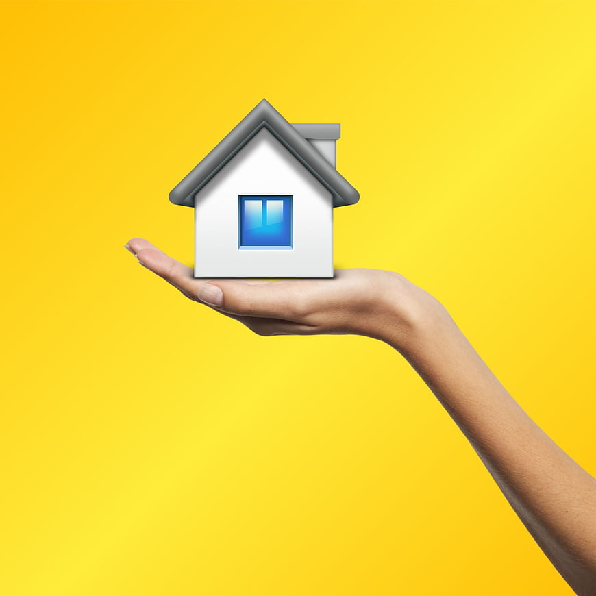 Hand holding miniature house model on yellow background