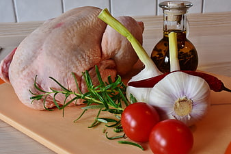 Raw whole chicken with garlic, rosemary, tomatoes, and oil