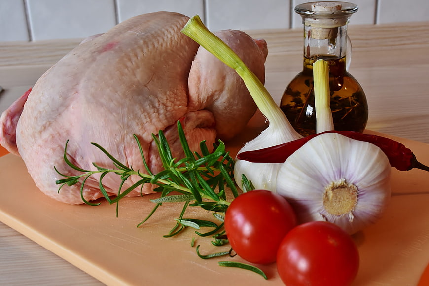 Raw whole chicken with garlic, rosemary, tomatoes, and oil