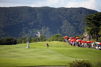 Golf tournament on a scenic course with spectators and red umbrellas