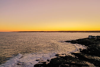 Serene Sunset Over Rocky Coastal Shoreline with Ocean Waves