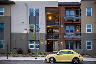 Yellow Volkswagen Beetle parked in front of modern apartment complex