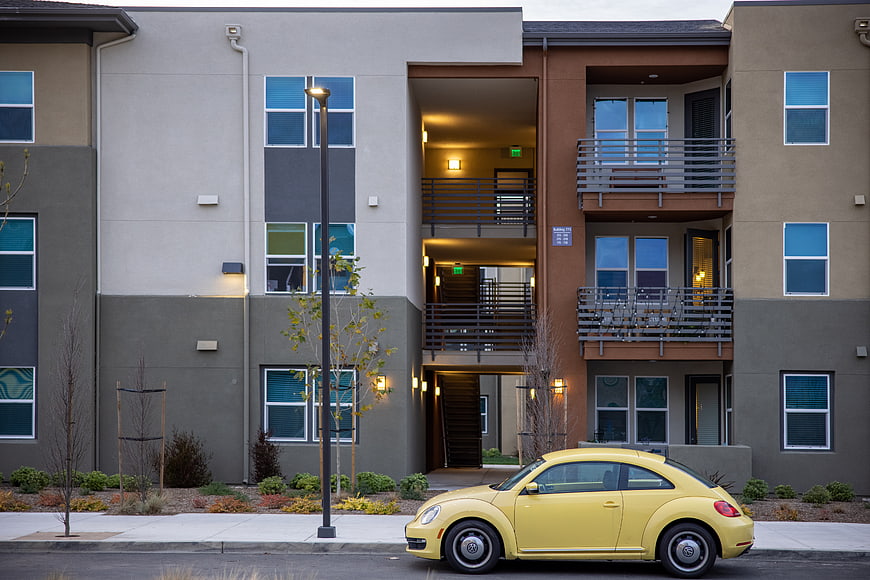 Yellow Volkswagen Beetle parked in front of modern apartment complex