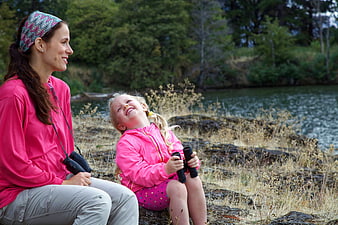 Happy mother and daughter laughing outdoors with binoculars
