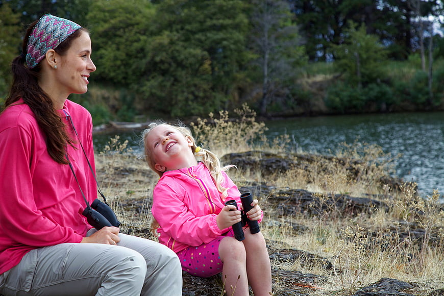 Happy mother and daughter laughing outdoors with binoculars