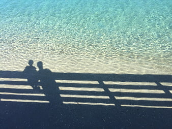 Shadows of couple on pier over turquoise water