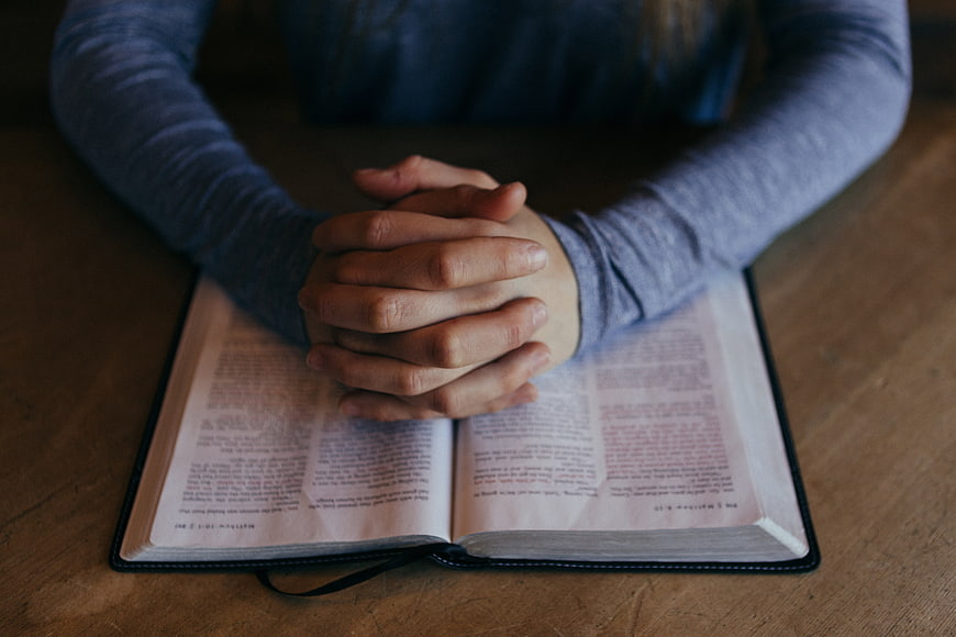 Hands Praying Over Open Bible on Wooden Table