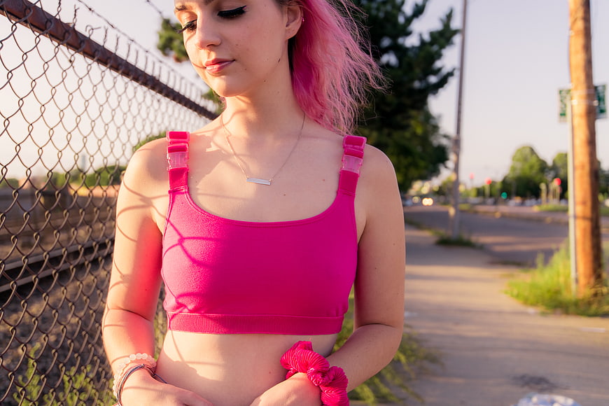 Young Woman with Pink Hair in Sports Bra by Fence