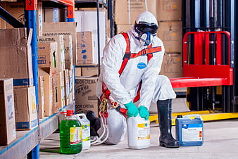 Worker in protective gear handling chemicals in warehouse