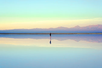 Woman standing in reflective lake with mountain sunset background