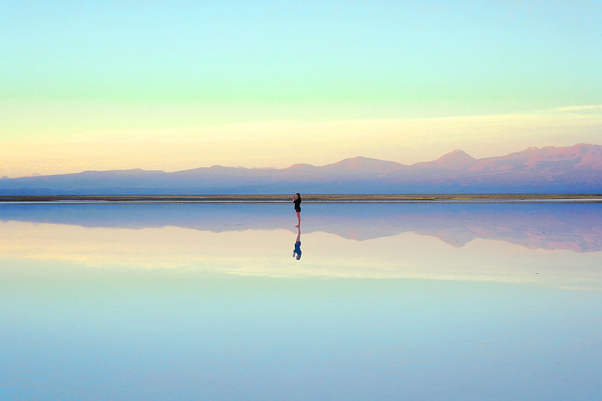 Woman standing in reflective lake with mountain sunset background