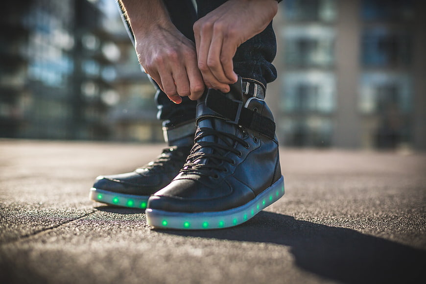 Person tying black sneakers with glowing green LED soles