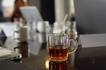 Glass mug of tea on office desk with blurred background