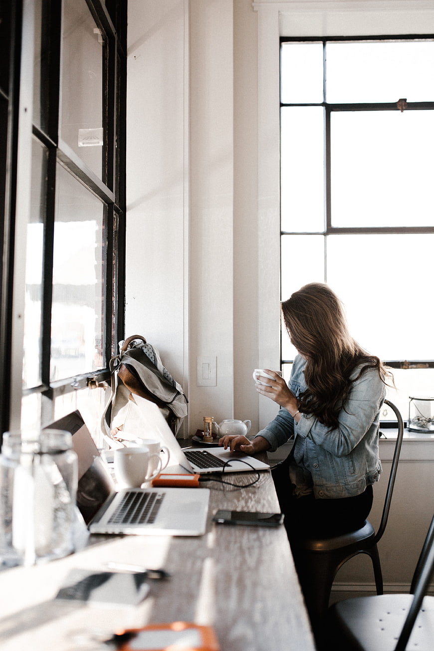 Woman working on laptop in bright office with coffee