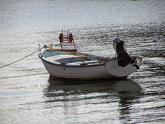 Small white fishing boat with outboard motor floating on calm water