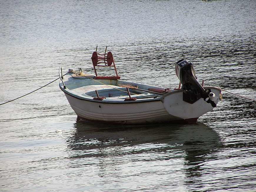 Small white fishing boat with outboard motor floating on calm water