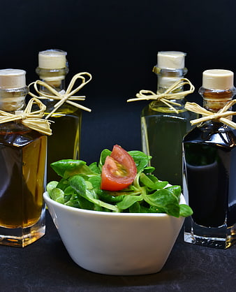 Fresh green salad with tomato and assorted oil bottles on dark background