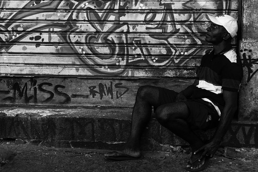 Black and white portrait of man sitting against graffiti wall