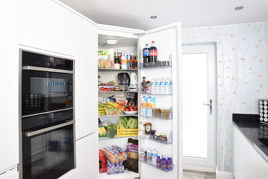 Open Refrigerator Filled With Fresh Food In Modern White Kitchen