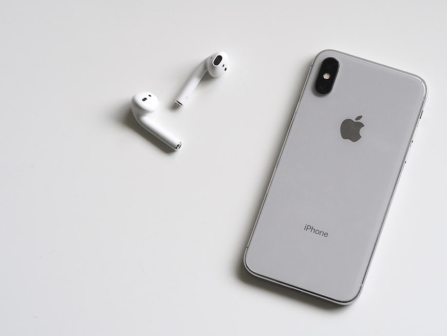Silver iPhone and White Wireless Earbuds on White Background
