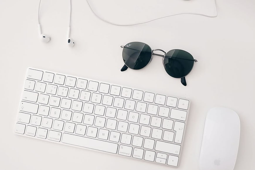 Minimalist White Desk Setup with Keyboard, Mouse, and Sunglasses