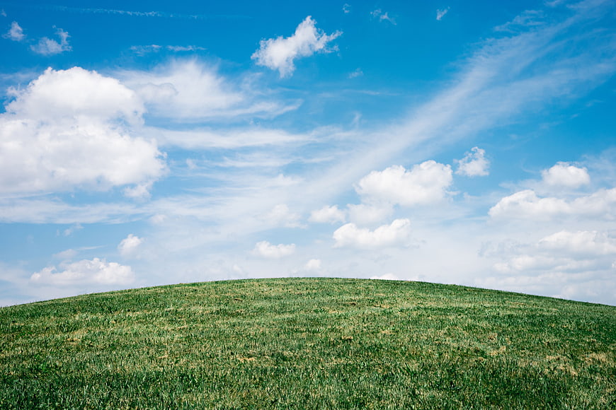 Green grassy hill under blue sky with white clouds