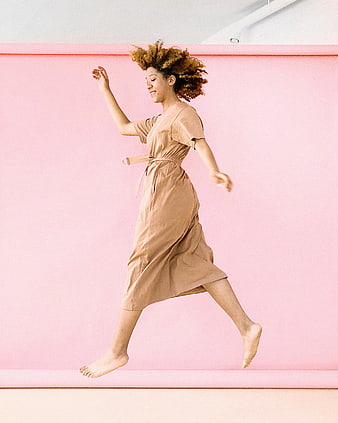 Joyful Woman Jumping in Beige Dress Against Pink Background