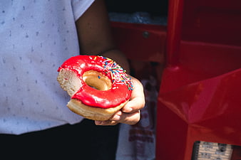 Hand holding red glazed donut with sprinkles
