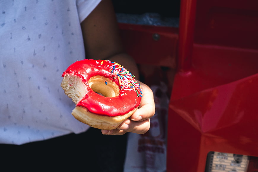 Hand holding red glazed donut with sprinkles