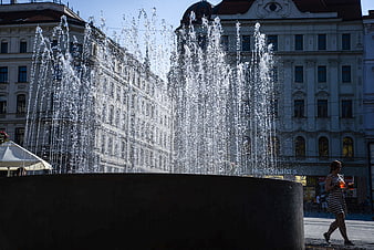 Woman walking past city fountain with water spray