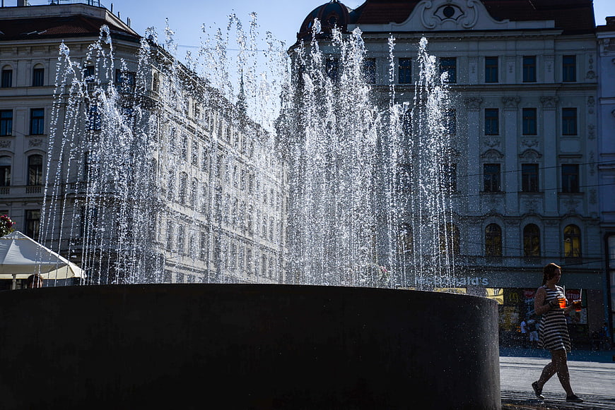 Woman walking past city fountain with water spray