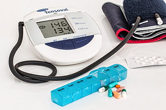 Blood Pressure Monitor, Weekly Pill Organizer, and Medication on White Surface
