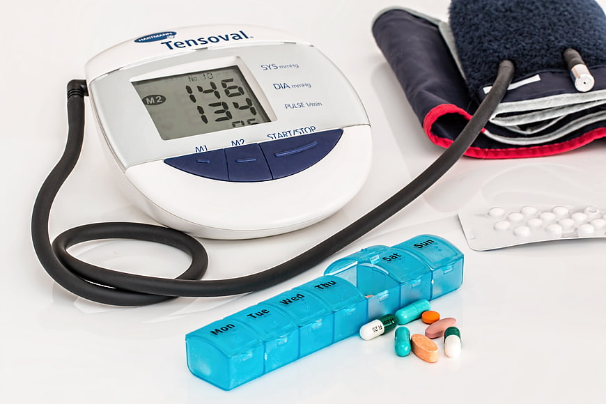 Blood Pressure Monitor, Weekly Pill Organizer, and Medication on White Surface