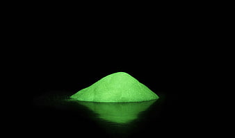Glowing green phosphorescent powder pile on black background