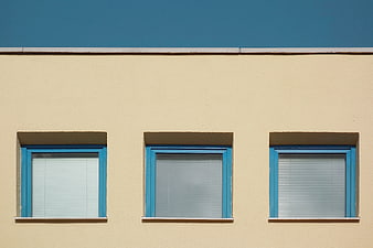 Minimalist beige building facade with three blue windows