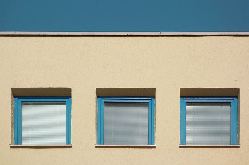 Minimalist beige building facade with three blue windows