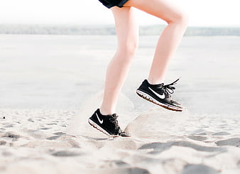 Woman Jumping in Sneakers on Sandy Beach